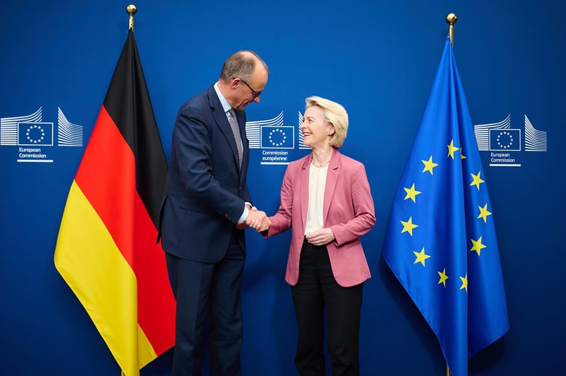 Friedrich Merz i Ursula von der Leyen ściskają sobie dłonie na tle flag Niemiec i Unii Europejskiej.